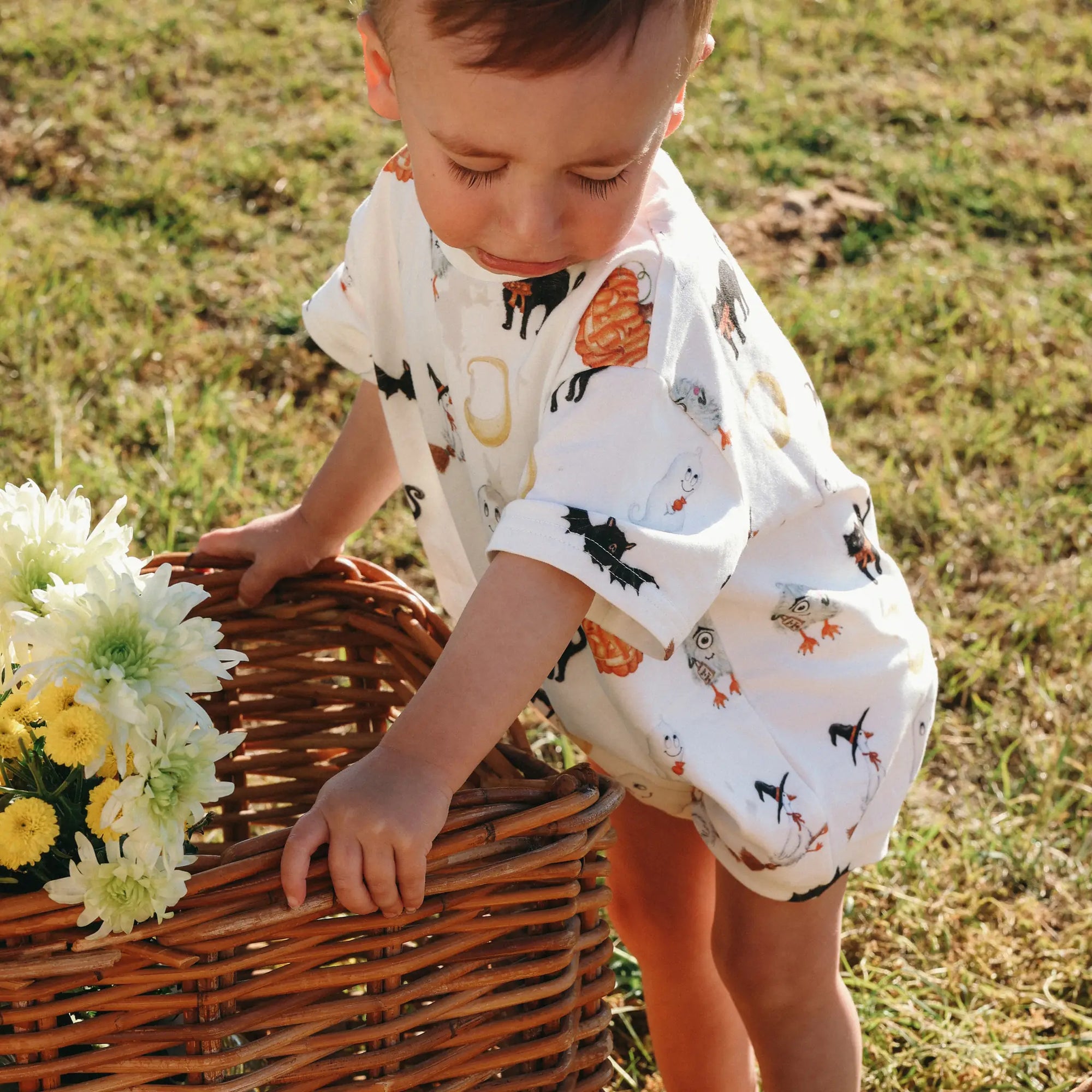 Baby in a Halloween print bubble romper leaning over a wicker basket of yellow and white flowers