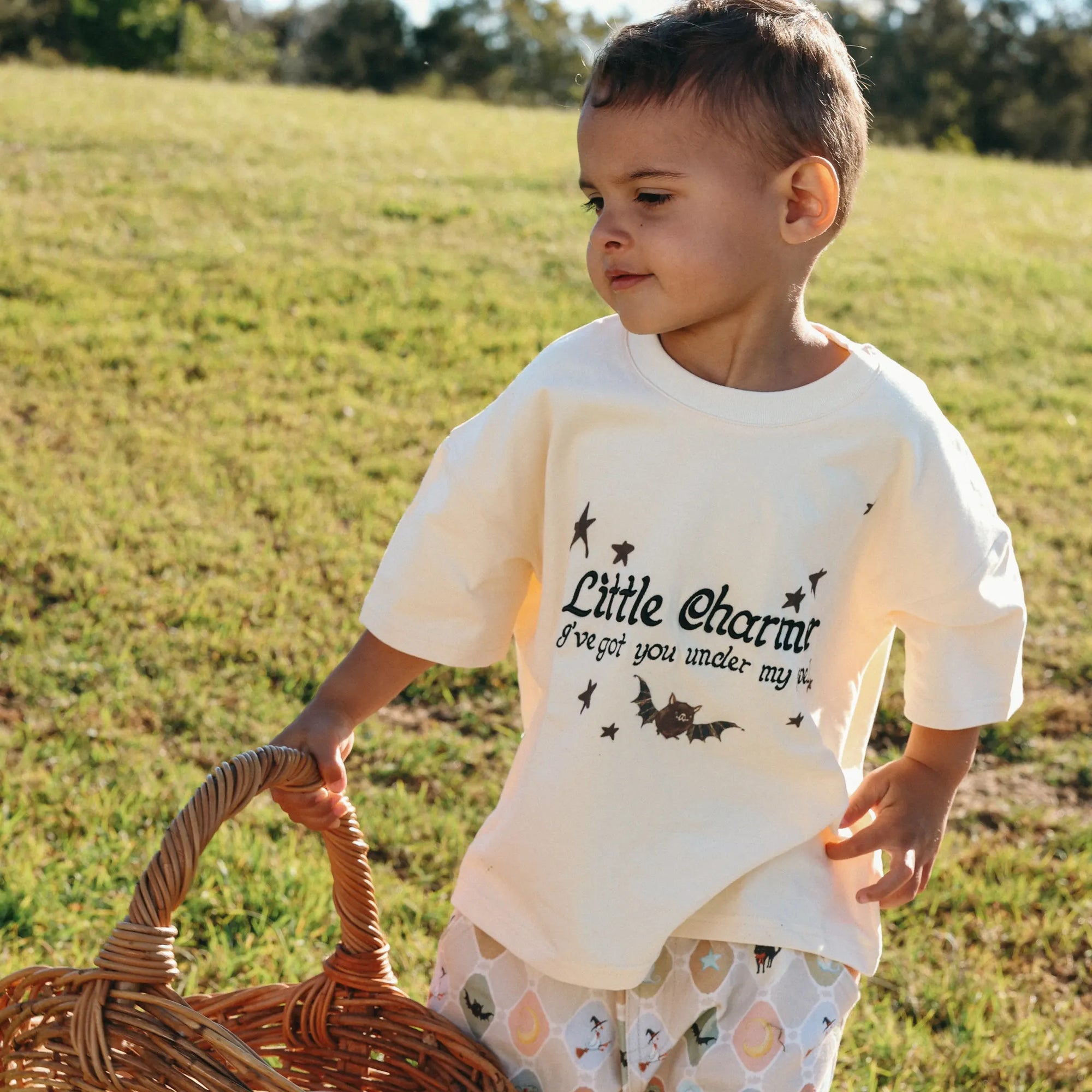 Toddler carrying a wicker basket in a Little Charmer tee and ghost print Halloween pants
