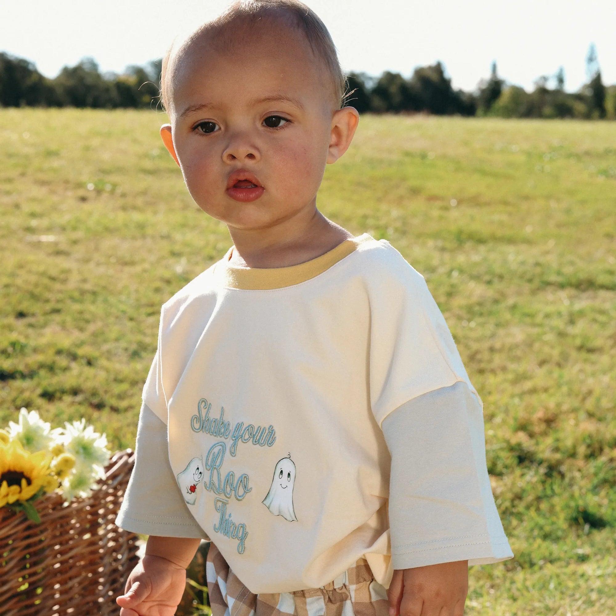Toddler in a Shake Your Boo Thing ghost print tee standing beside a basket of sunflowers