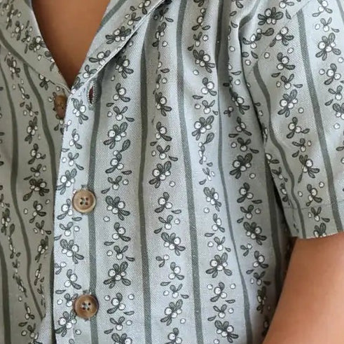 Close-up of a boy's sage green Holly Berry Stripe pyjama shirt with a camp collar and timber buttons