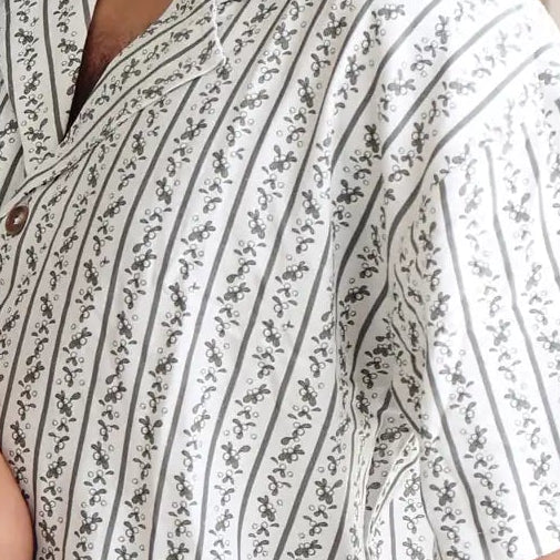 Dad and toddler smiling at each other in matching botanical print Christmas pyjamas beside a lit tree