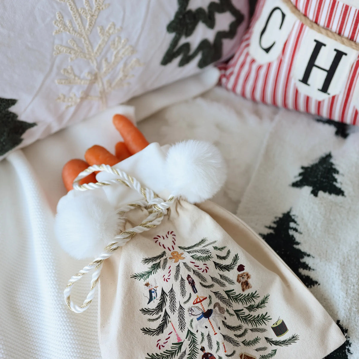 Embroidered Christmas tree print Santa sack with a white cord drawstring and pom poms, filled with carrots on a knit throw