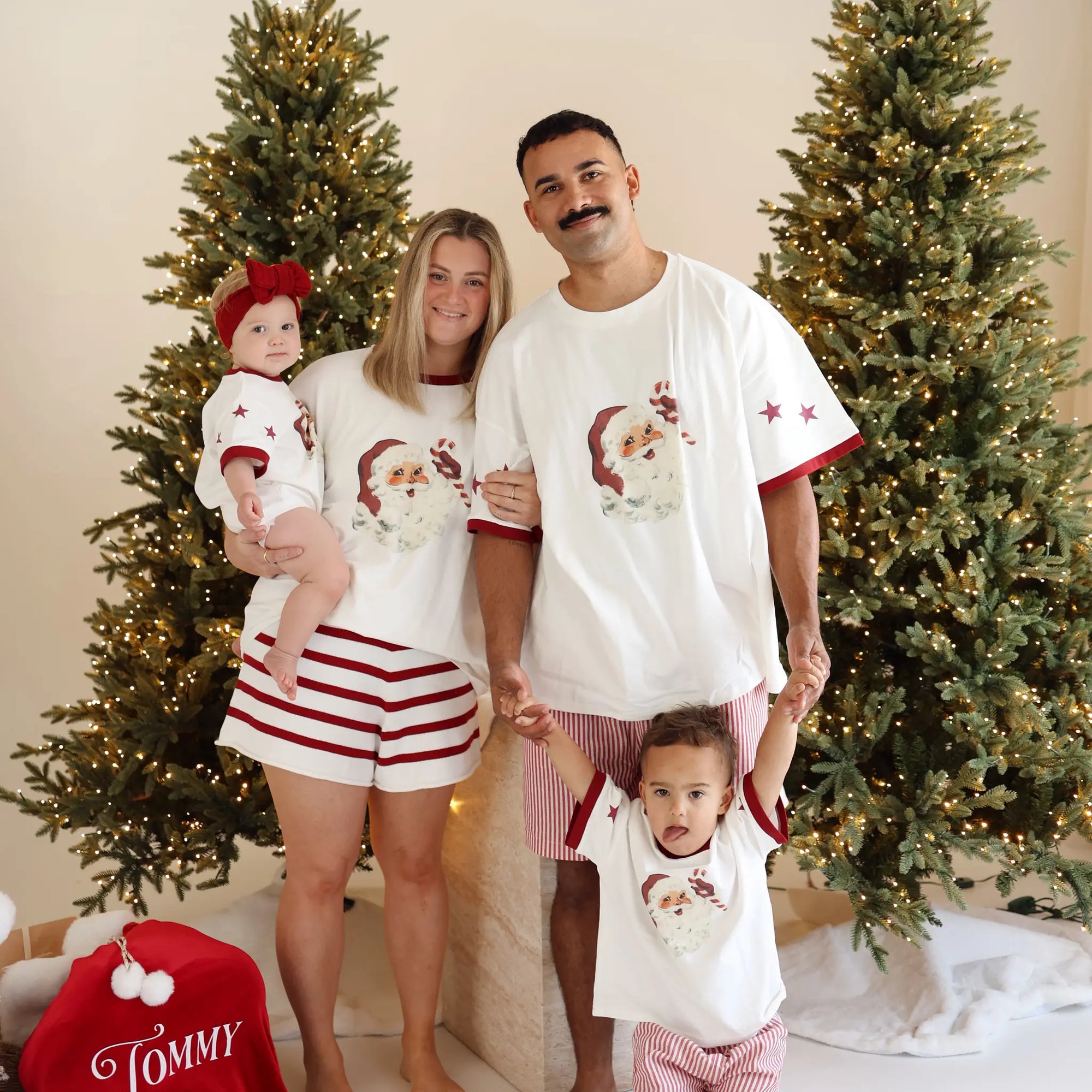Family of four in matching vintage Santa print pyjamas beside a personalised red Santa sack embroidered with the name Tommy