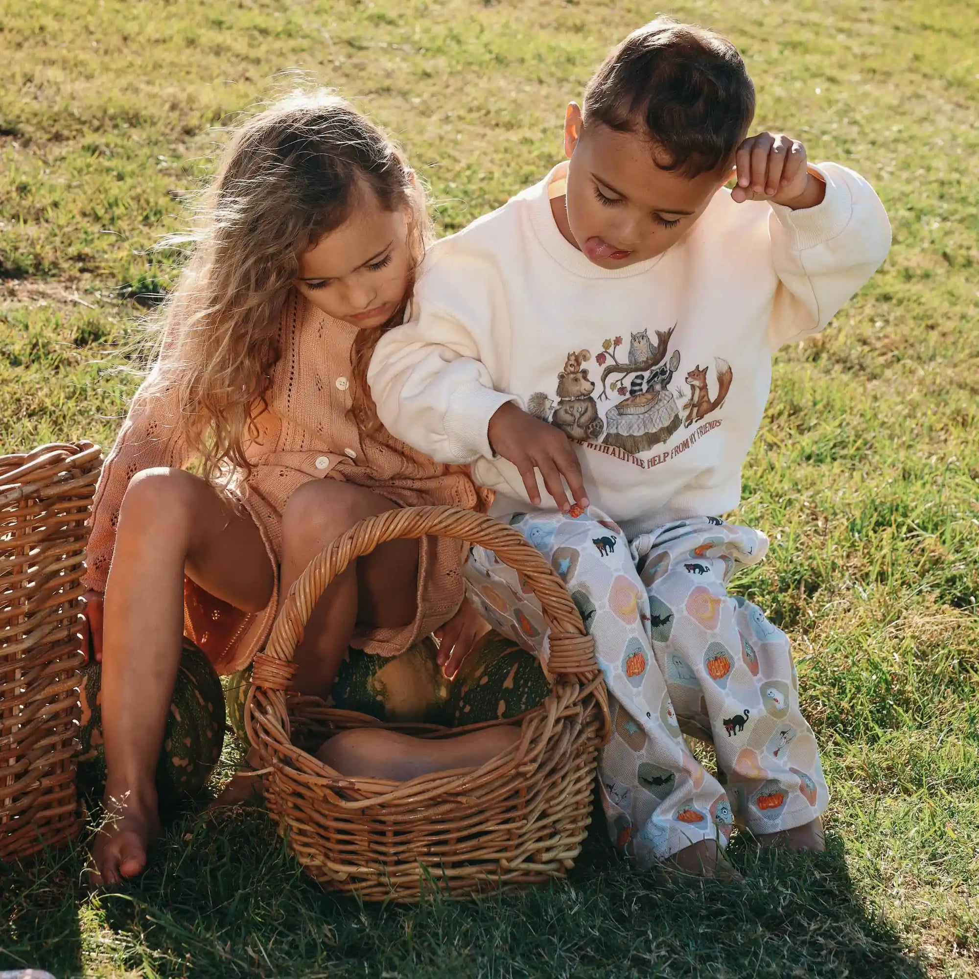 Girl in an apricot floral set beside a boy in a woodland animals sweatshirt and Halloween print pants