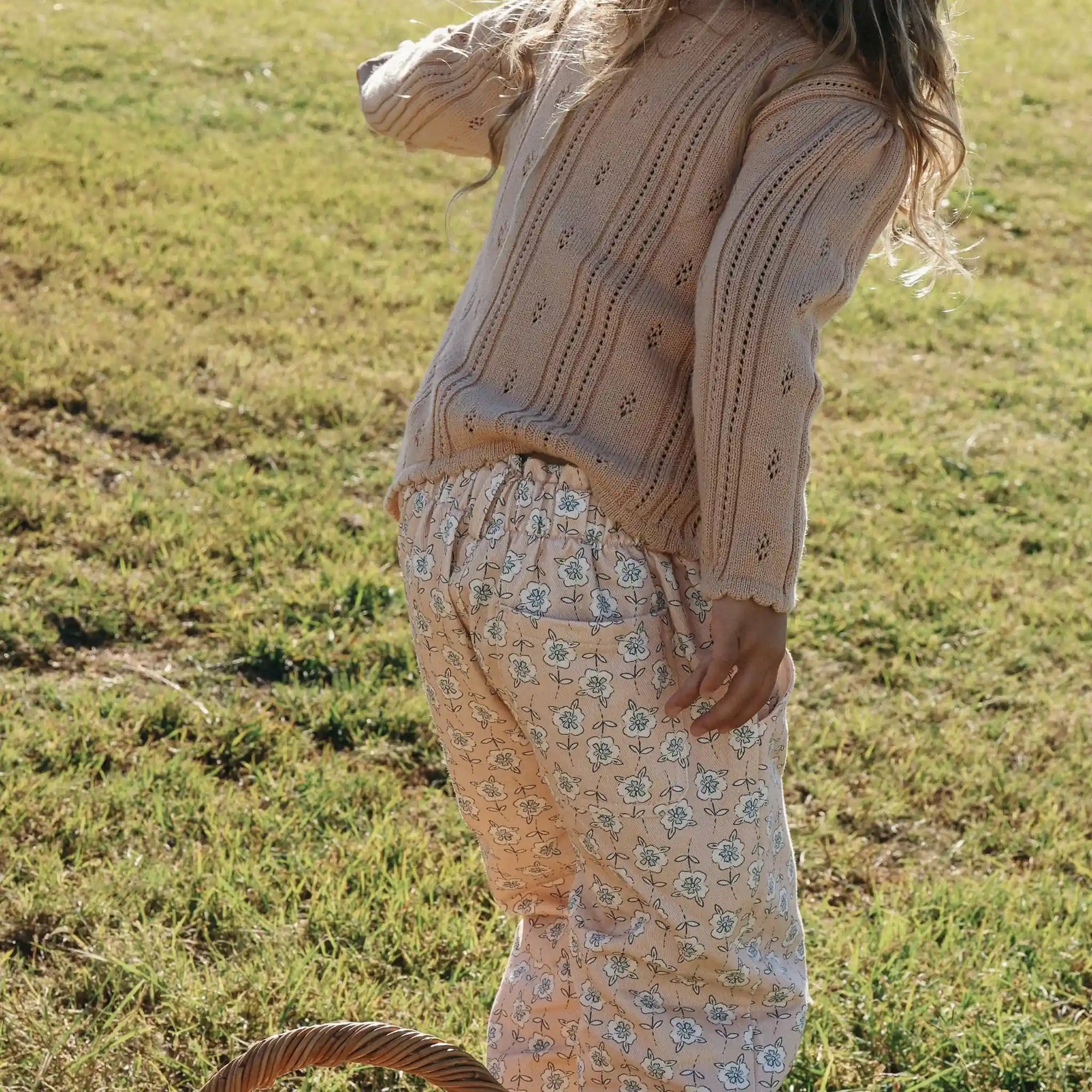 Side view of a girl in a cream pointelle knit cardigan and apricot floral print pants