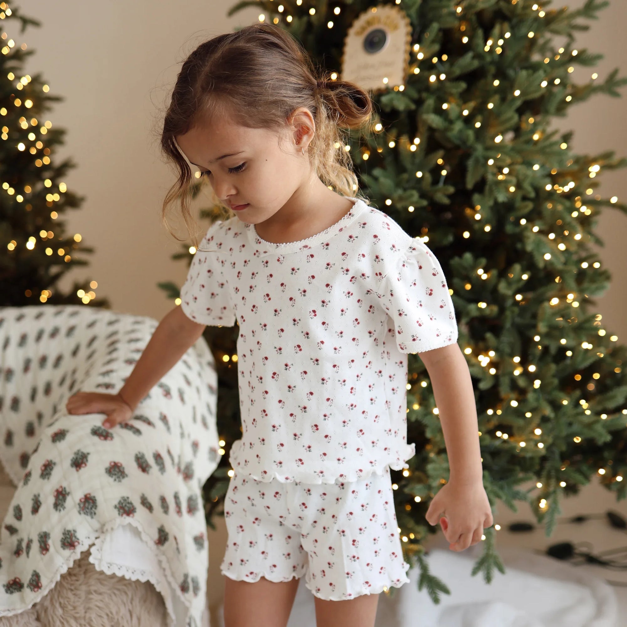 Girl in a cherry print puff sleeve pyjama set in front of a lit Christmas tree
