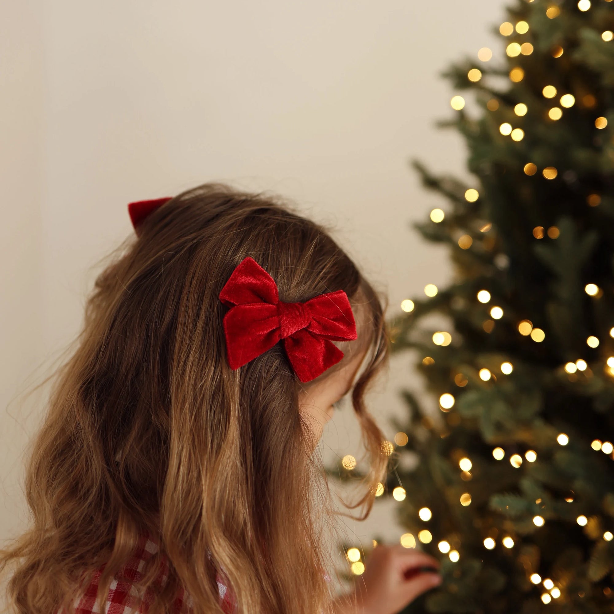 Close up of a red velvet hair bow clipped into a girl's hair beside a lit Christmas tree