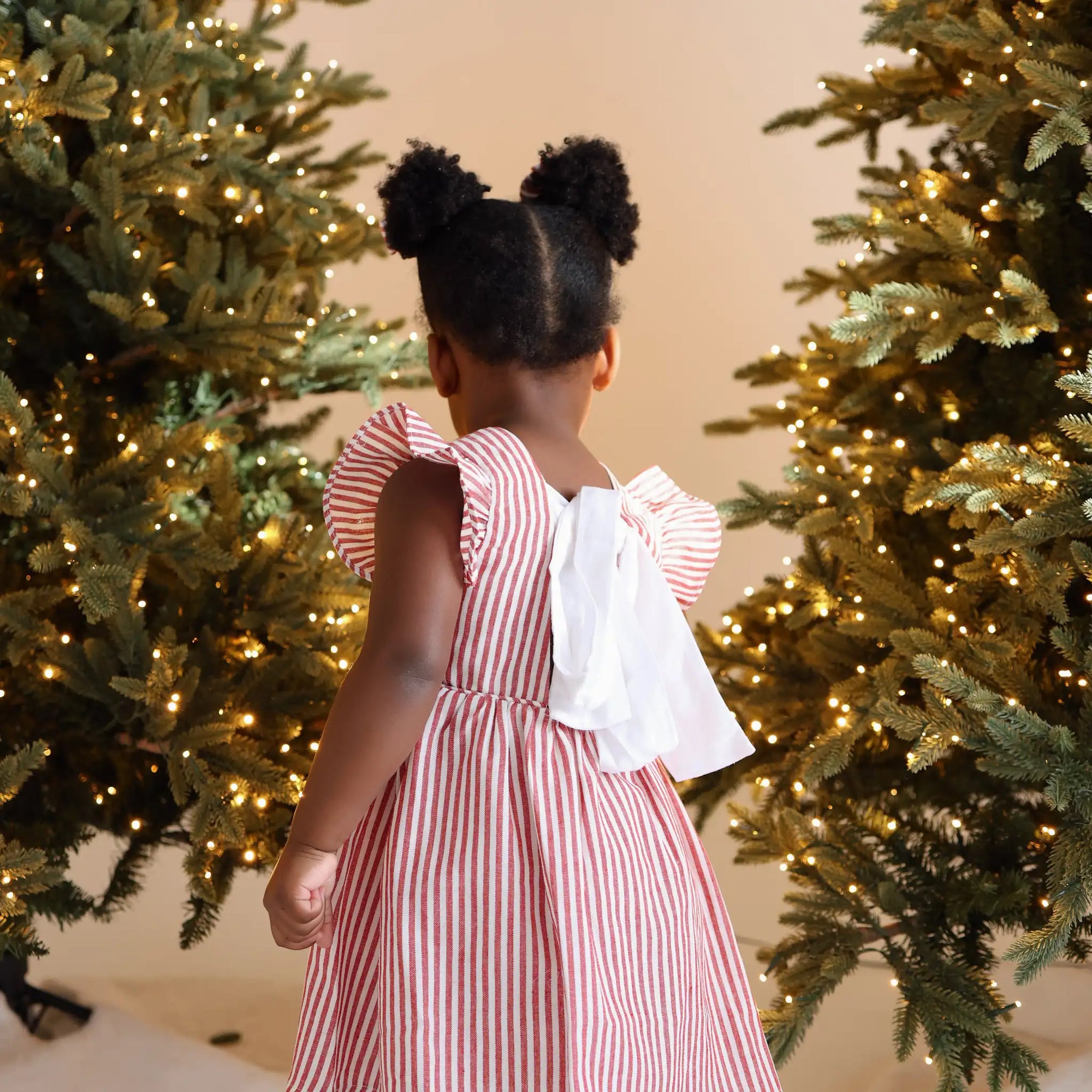 Back view of a toddler in a red and white stripe Christmas dress with a large white bow tie detail