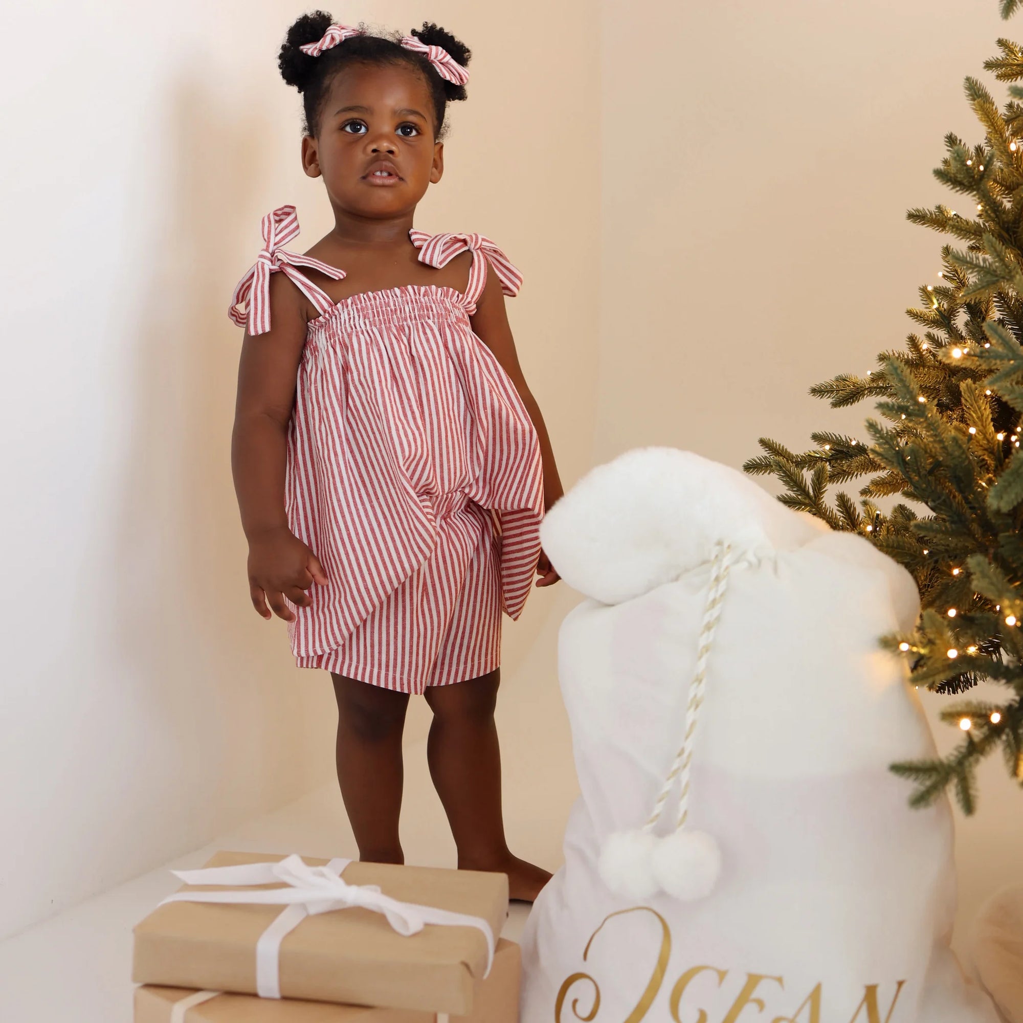 Toddler in a red stripe Christmas dress beside a personalised white Santa sack embroidered Ocean