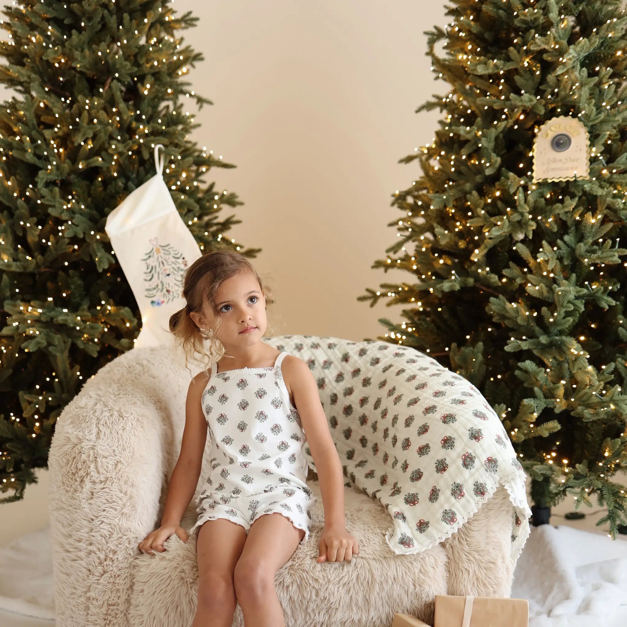 Girl in a wreath print singlet and shorts pyjama set on a sheepskin chair with a matching muslin wrap