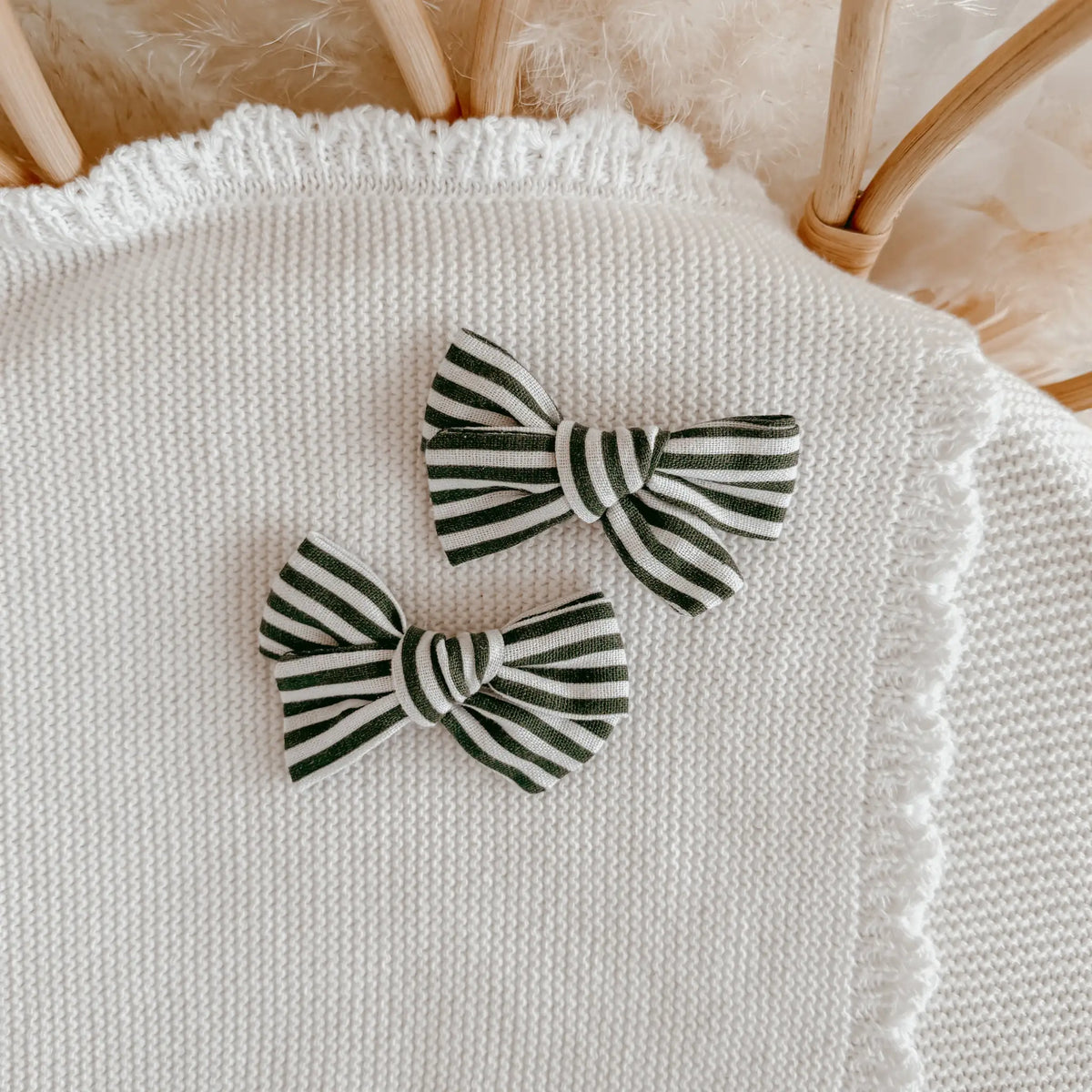 Two small fabric bow hair clips with dark green and off-white stripes, displayed on a white knit baby sweater.
