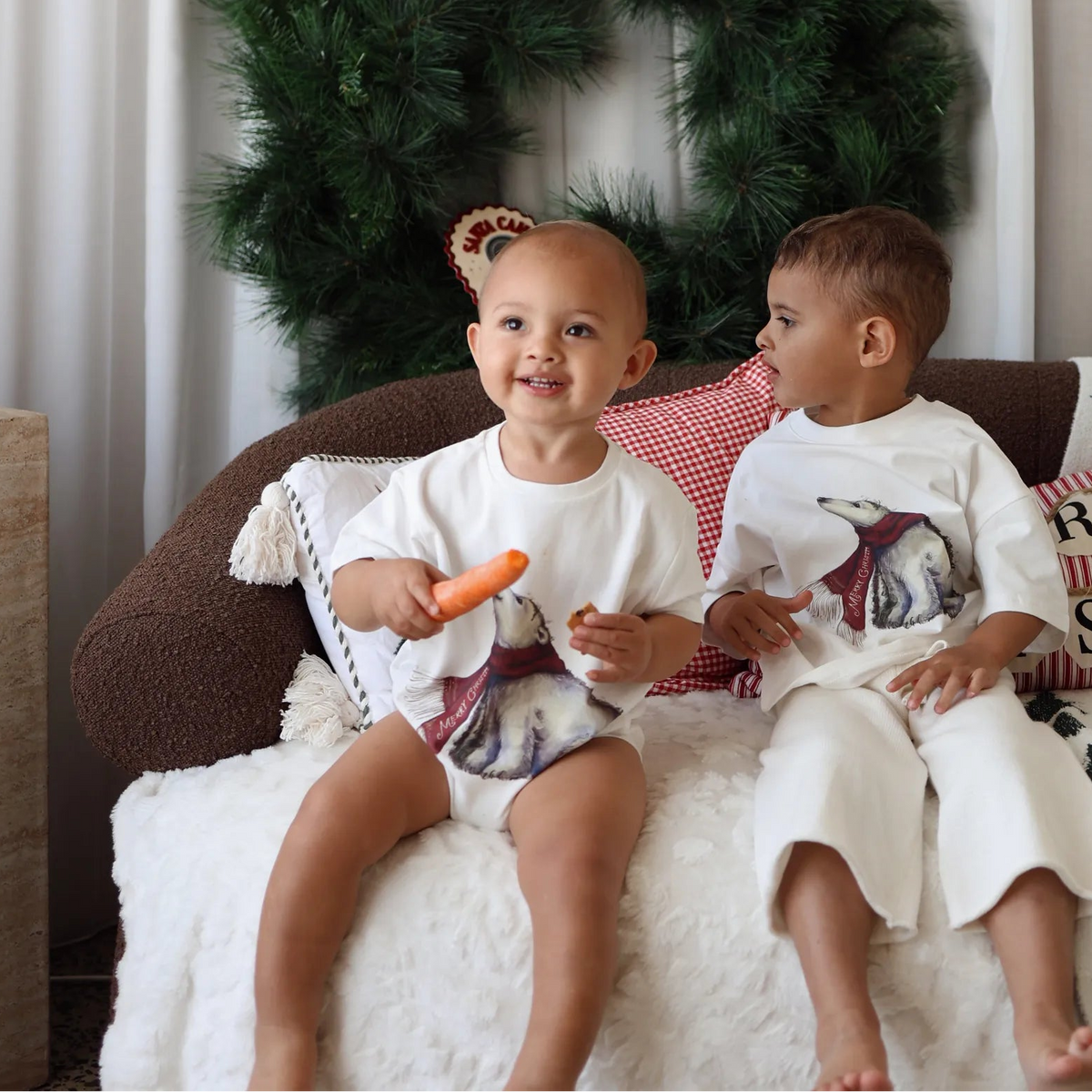 Two children in polar bear print sets on a sofa with a Christmas wreath and Merry Christmas cushions