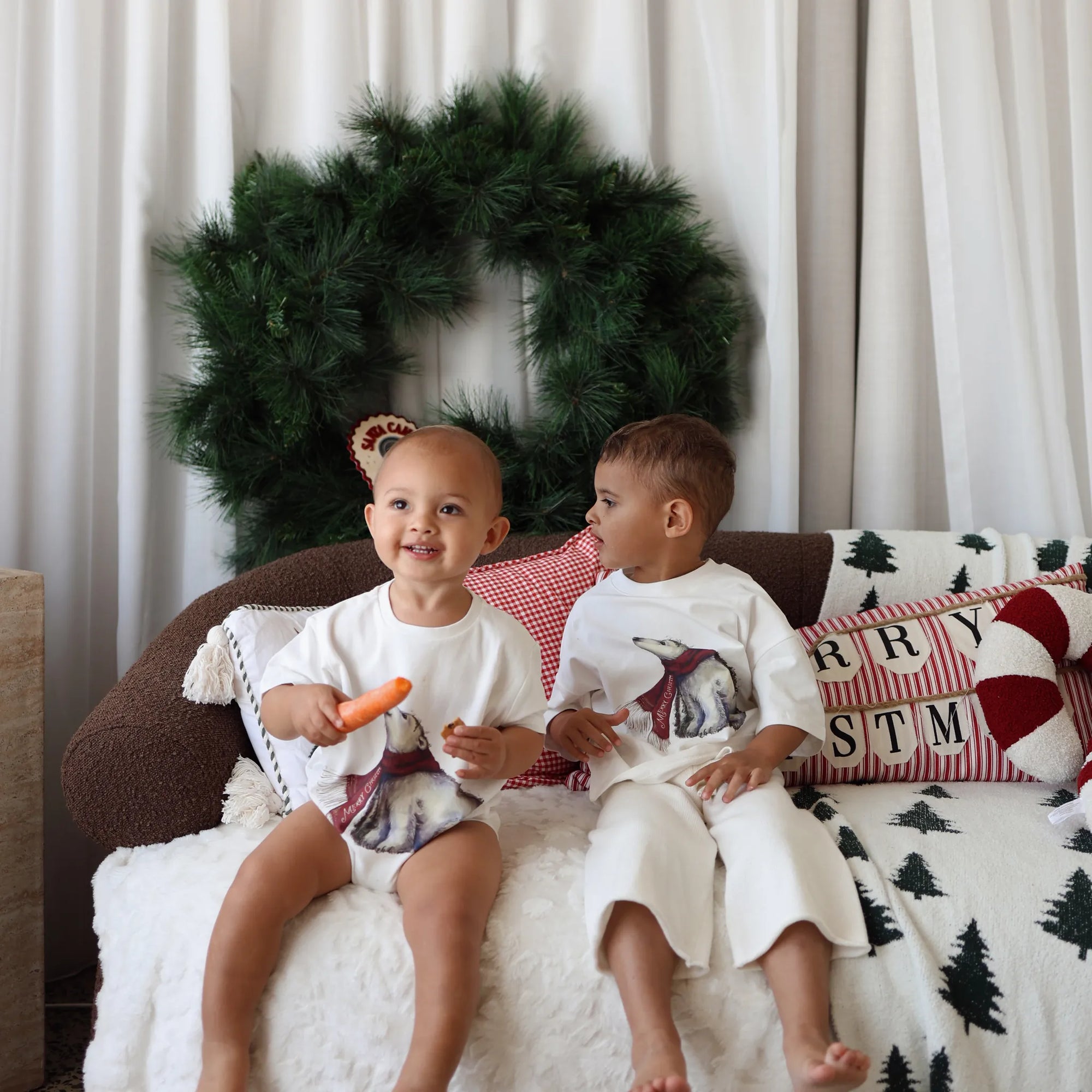 Two children in polar bear print sets on a sofa with a Christmas wreath and Merry Christmas cushions