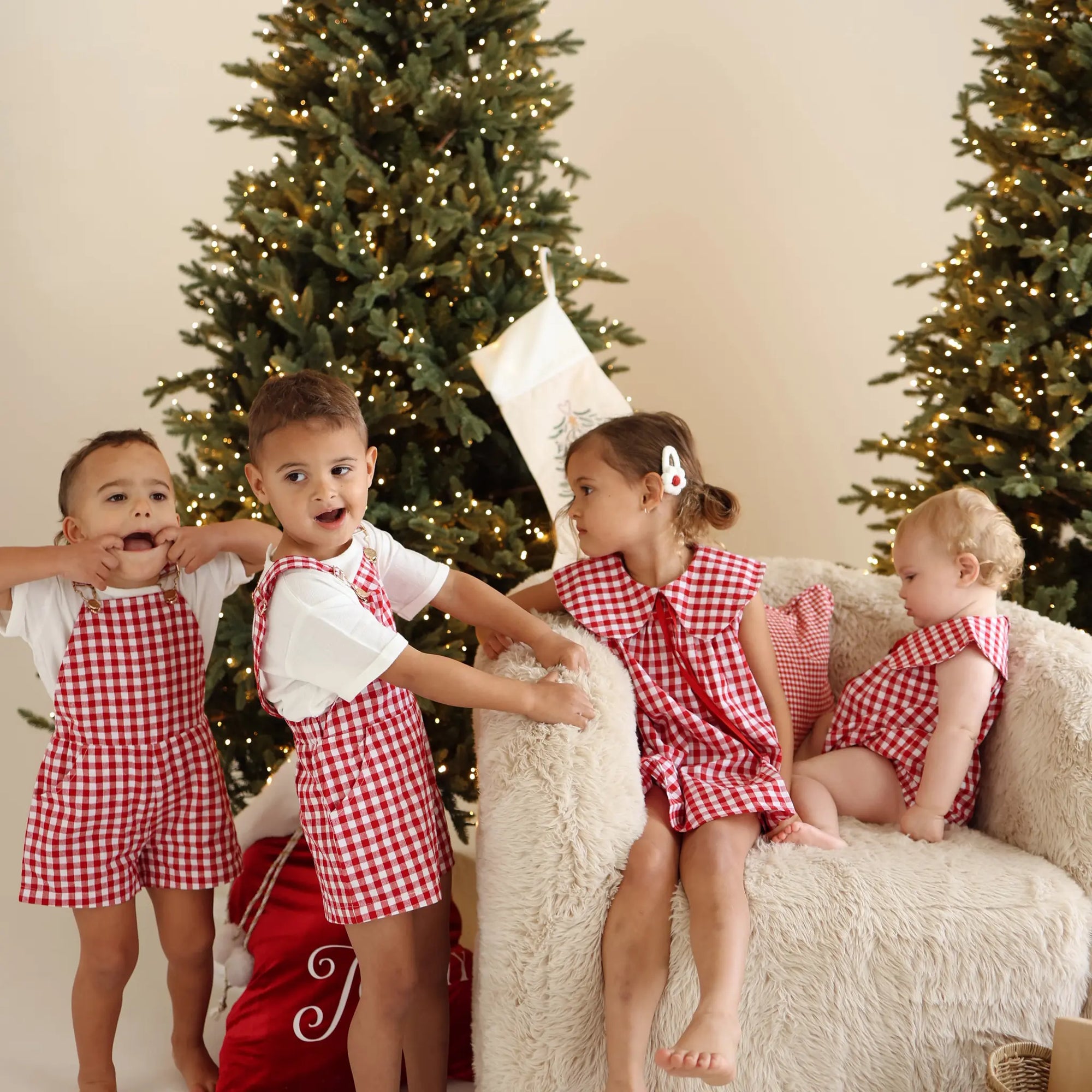 Four children in matching red gingham Christmas sets playing together between lit Christmas trees