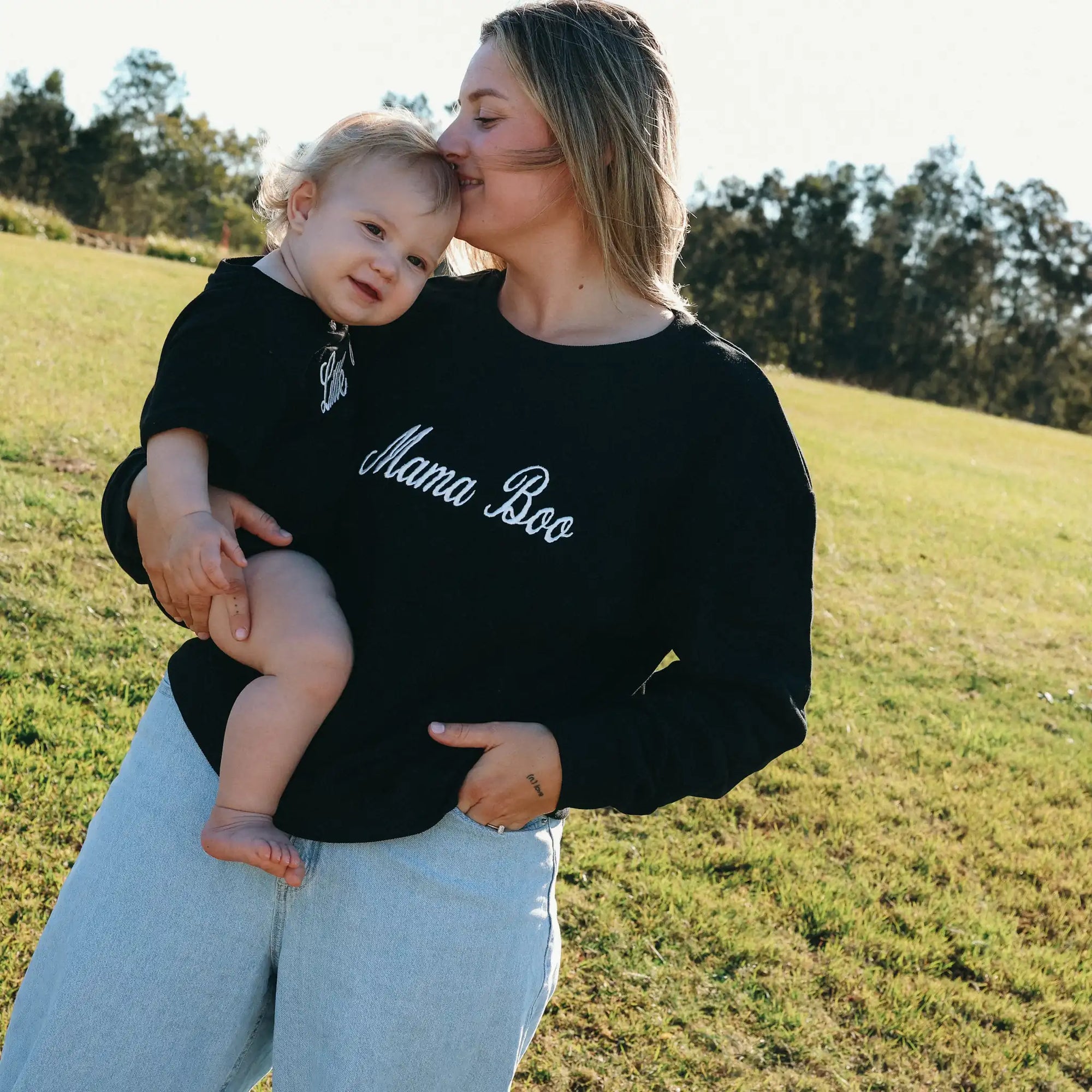 Mum kissing her baby's head, both in matching Mama Boo and Little Boo embroidered sweatshirts