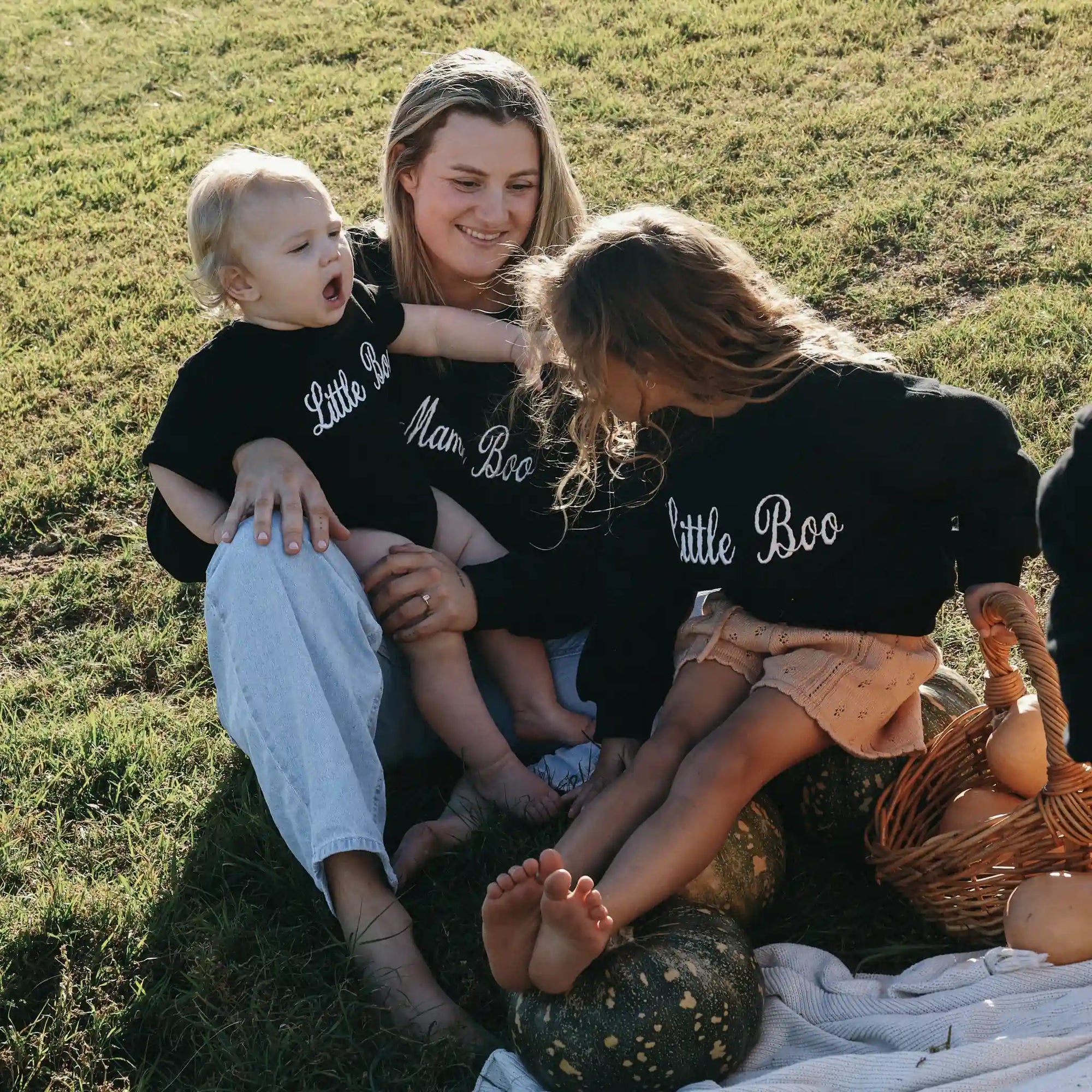 Mum and two children in matching Mama Boo and Little Boo sweatshirts sitting on the grass with pumpkins
