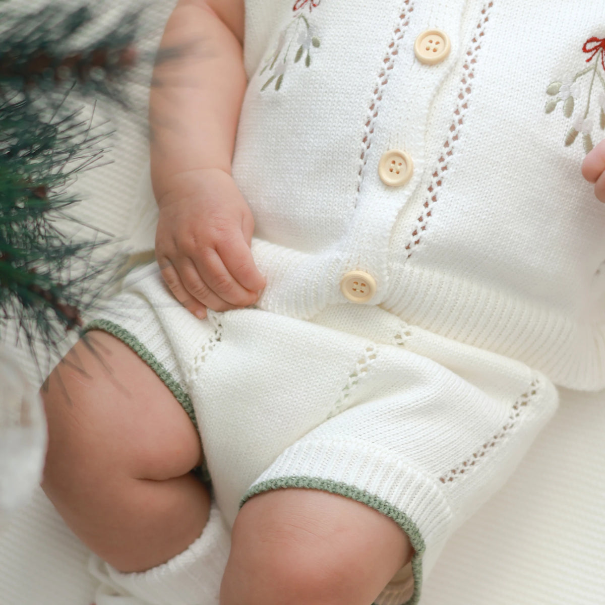 Close-up of white mistletoe knit shorts with green trim and pointelle detail, worn with the matching buttoned knit vest