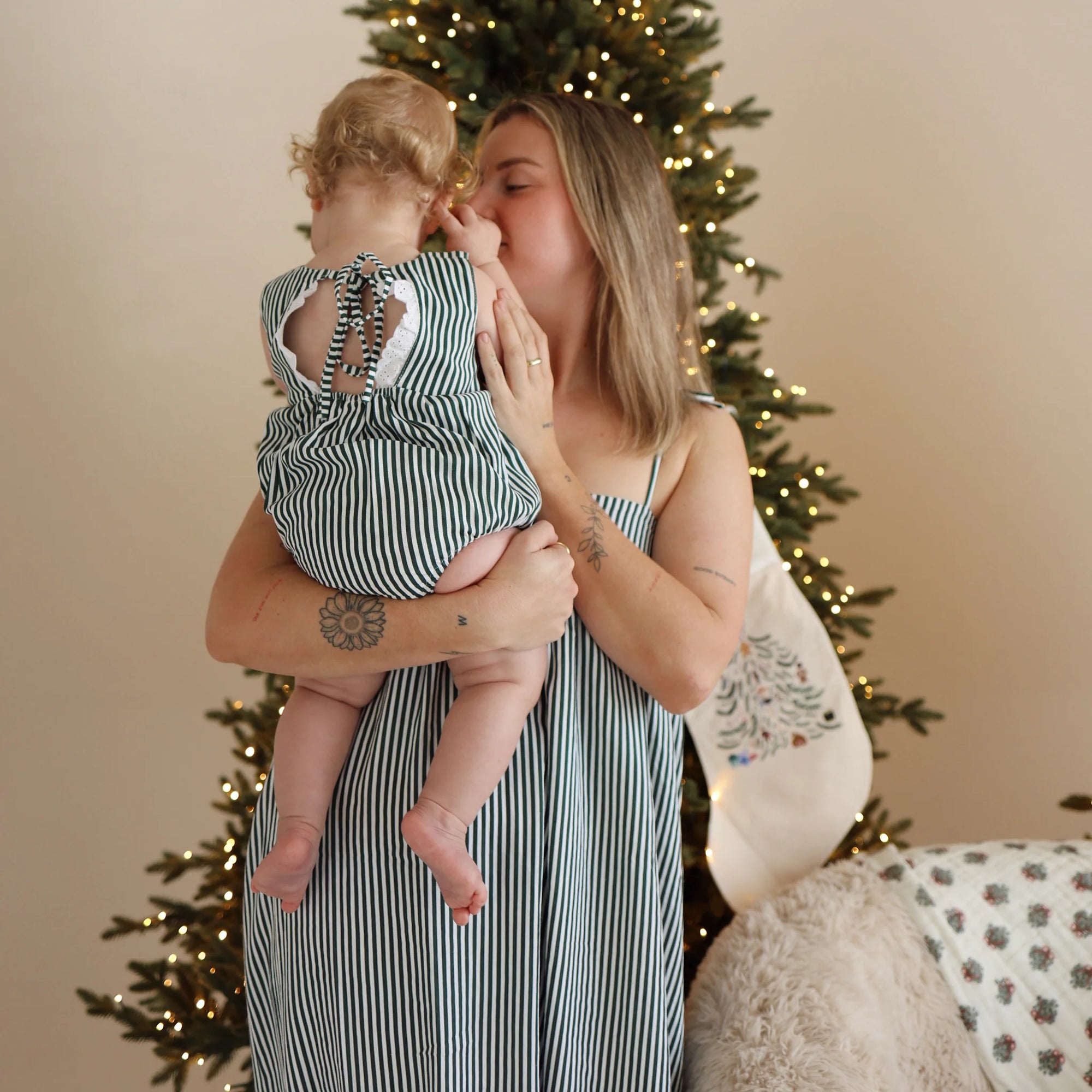 Mum kissing her baby, both in matching green stripe Christmas sets beside an embroidered stocking