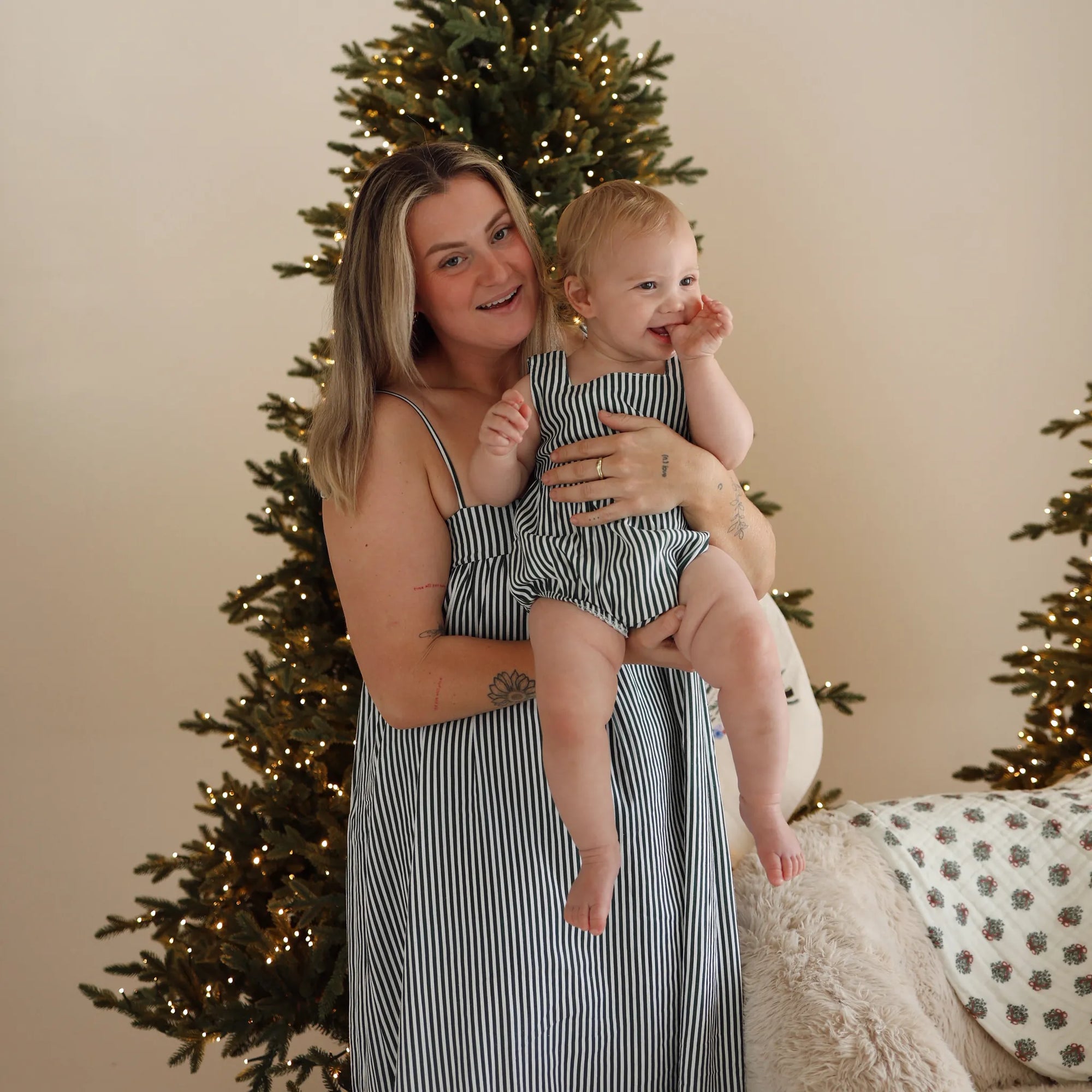 Mum holding a baby in matching green stripe Christmas sets, mum in a stripe maxi dress