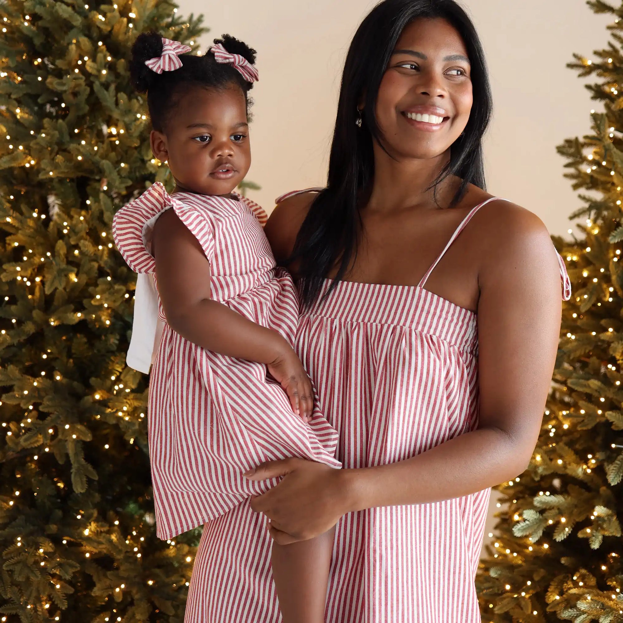 Mum holding her daughter in matching red and white stripe Christmas dresses, toddler wearing stripe hair bows