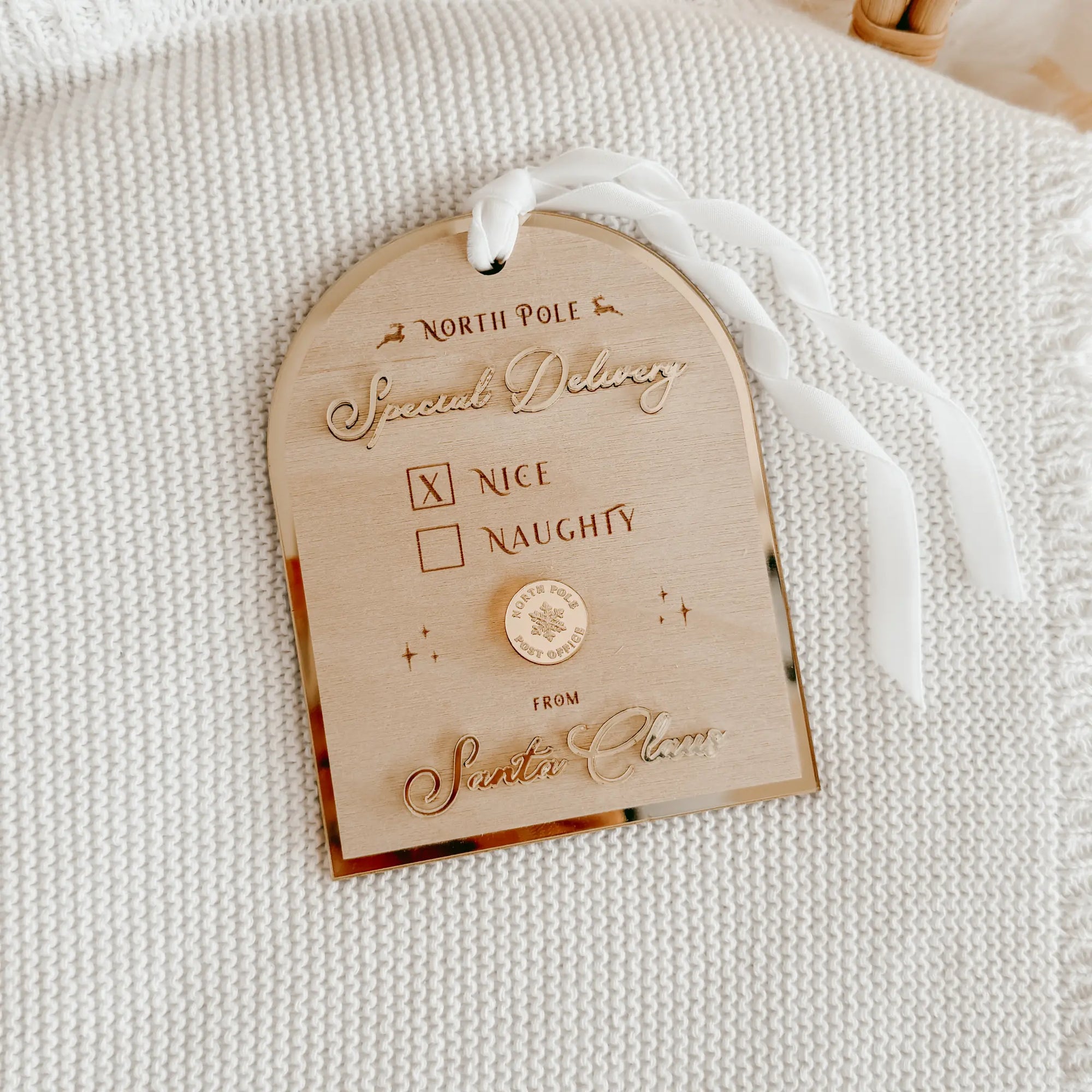 A personalized wooden advent tag with a white ribbon, featuring engraved text that reads 'NORTH POLE', 'Special Delivery', a checkbox marked 'X' next to 'NICE', and 'FROM Santa's Elves'.