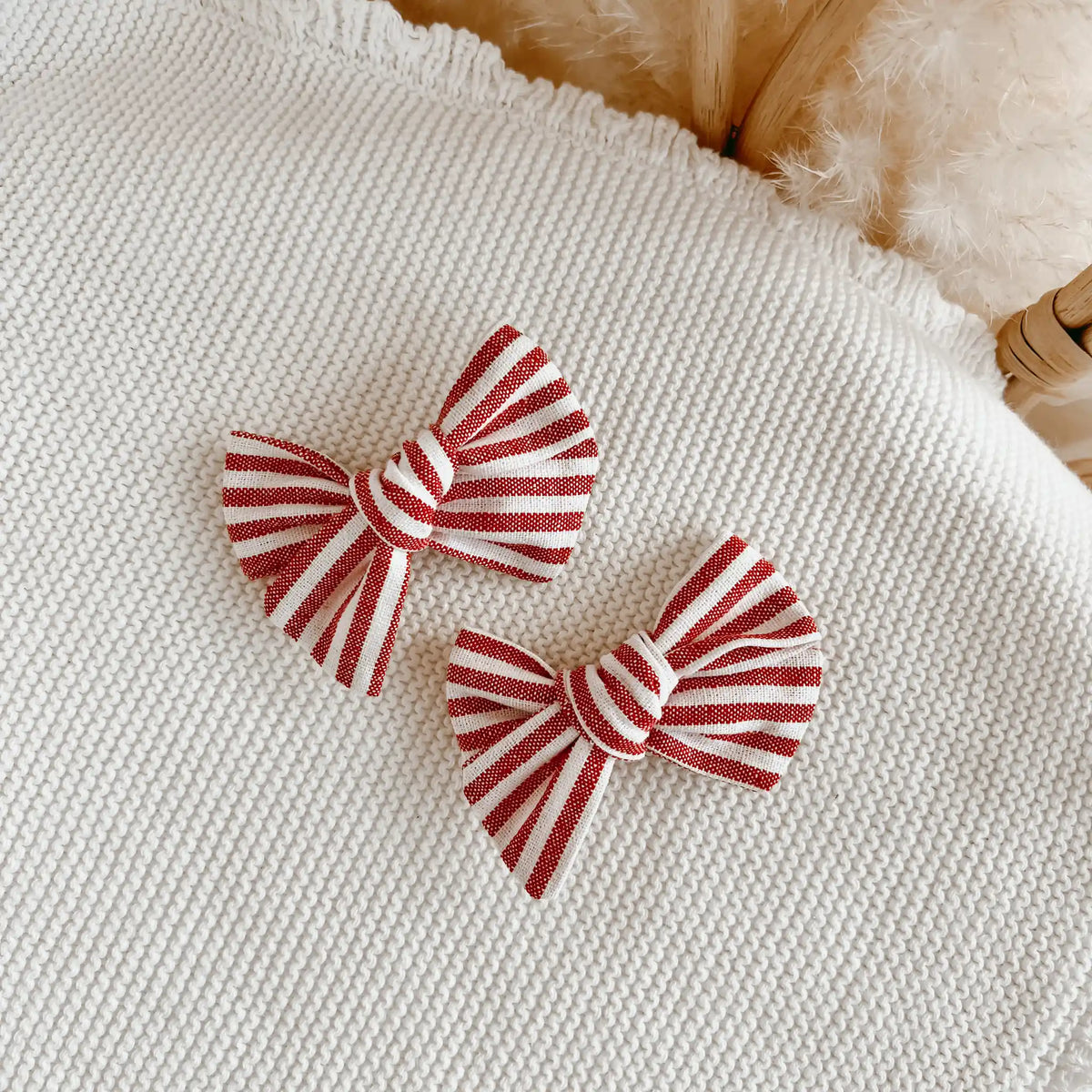 Pair of red and white stripe linen bow hair clips on a cream knit blanket