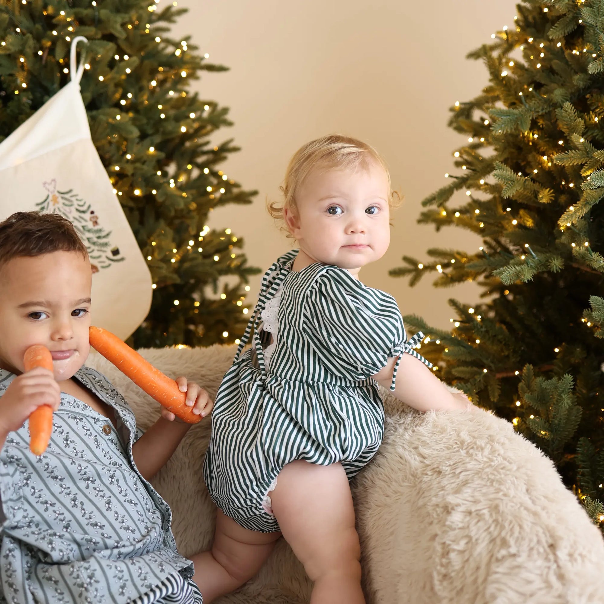 Two children in green stripe and botanical print Christmas sets holding carrots for the reindeer