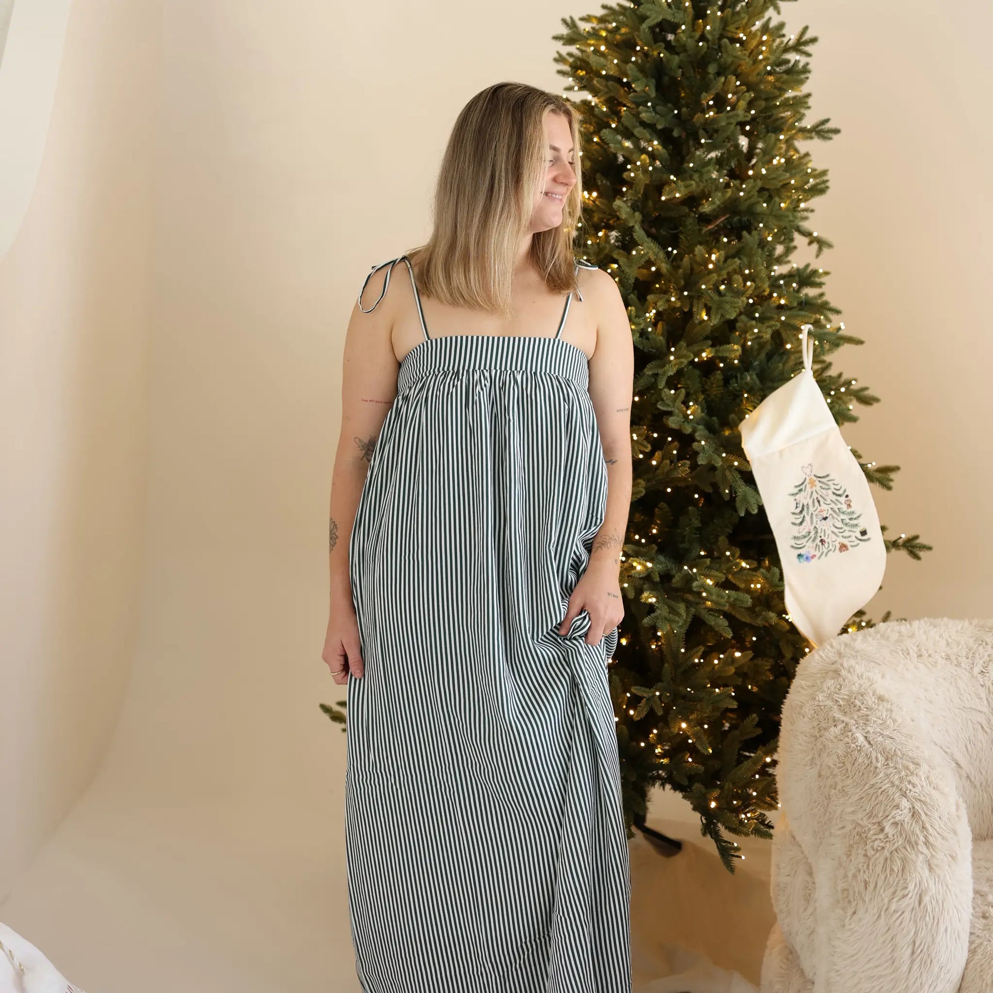 Woman in a green and white stripe shirred maxi Christmas dress beside an embroidered stocking