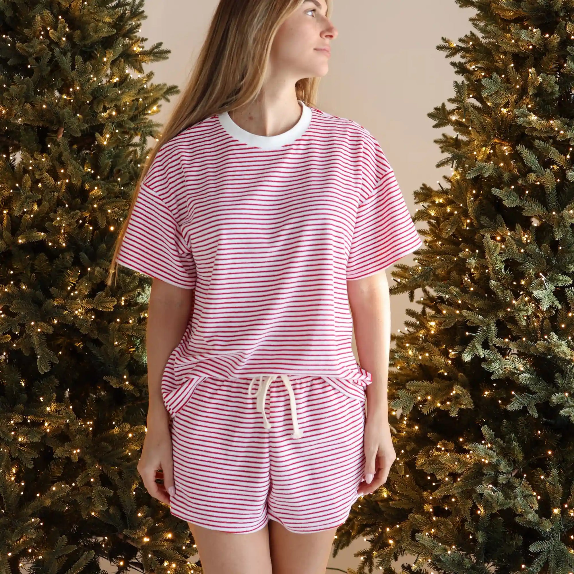 Woman in a red and white stripe tee and drawstring shorts pyjama set between two lit Christmas trees