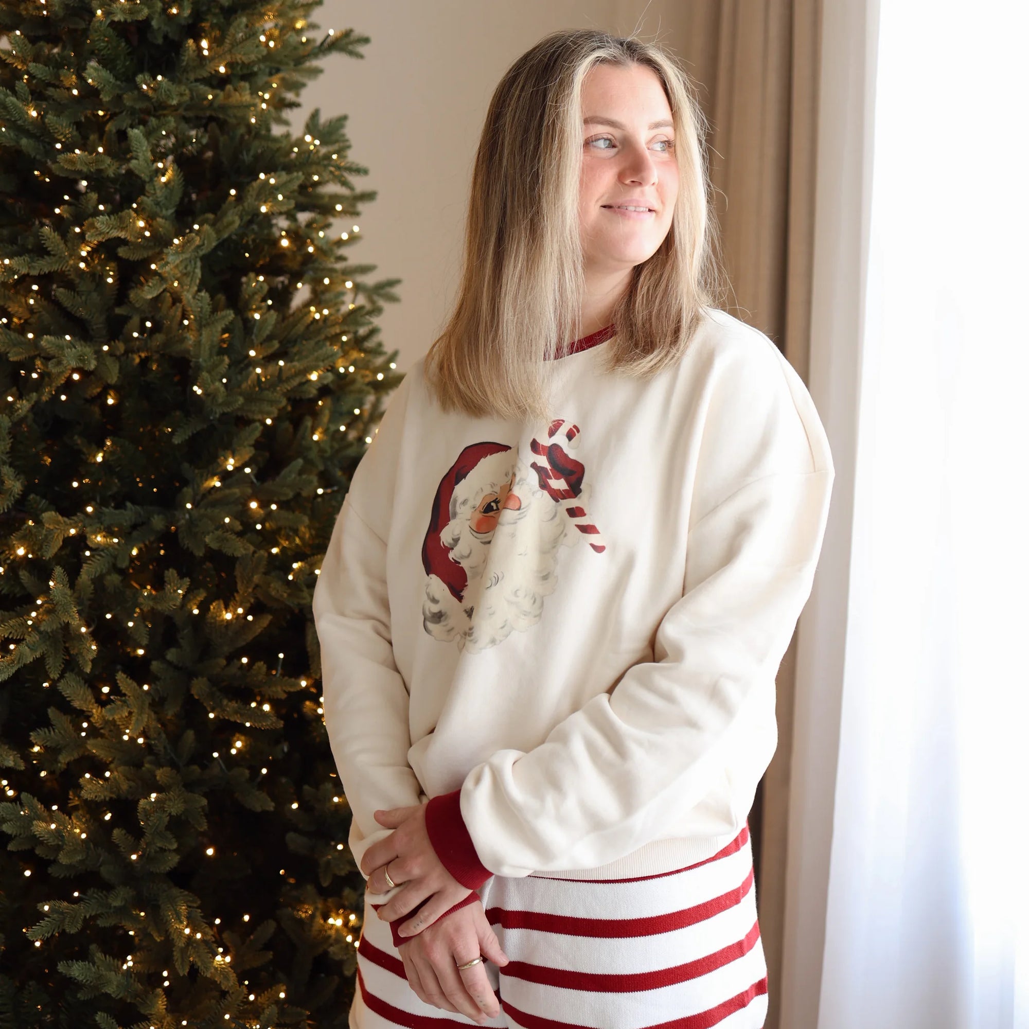 Woman in a vintage Santa print sweatshirt and red stripe knit shorts beside a lit Christmas tree